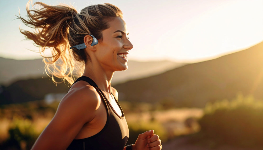 Woman running outdoors on an open trail wearing Drip-Fly OZ5 bone conduction headphones with mountains in the background